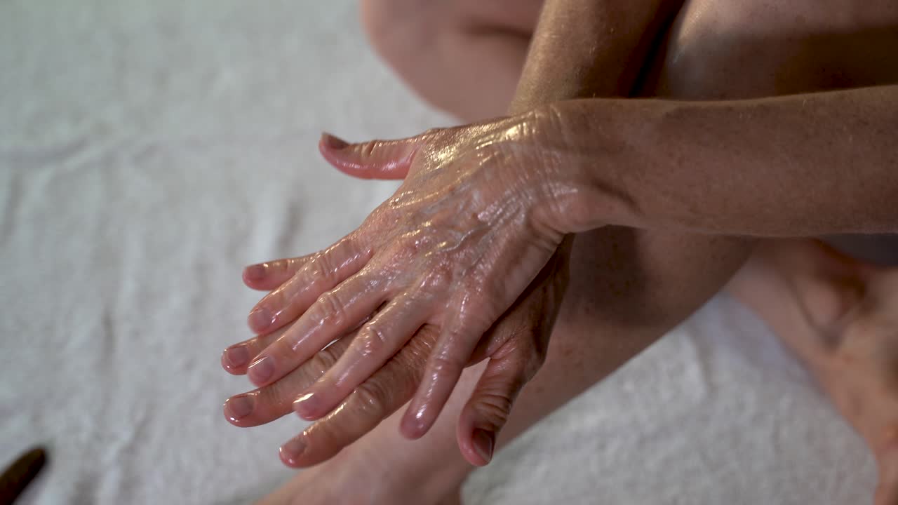 Primo piano di una donna matura che si spalma olio di cocco sulle mani preparandosi per un massaggio alle gambe