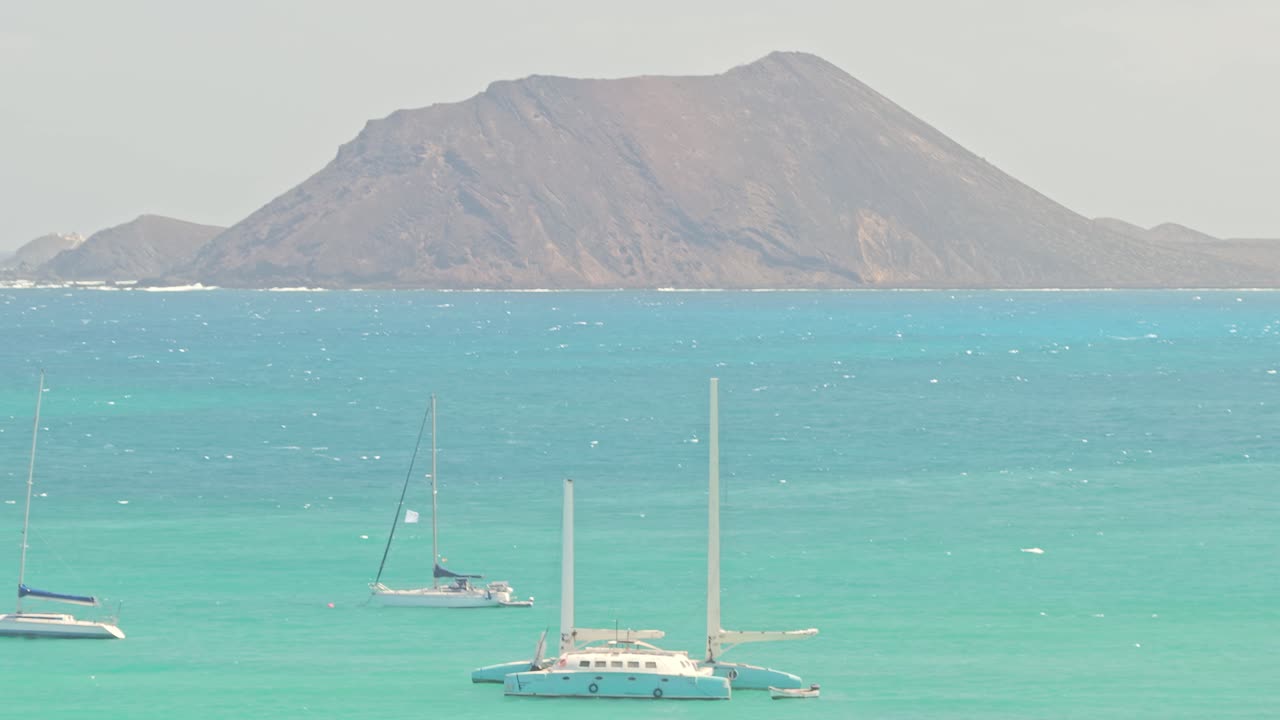 Drone captures Playa del Medio with turquoise waters anchored boats and rugged island backdrop showing secluded beach terrain and maritime calm on La Gomera’s southern coast