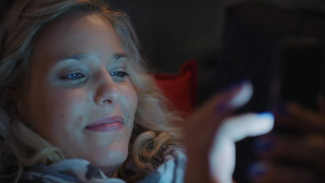 Smuk blond kvinde, der bruger smartphone-teknologi hjemme om natten.