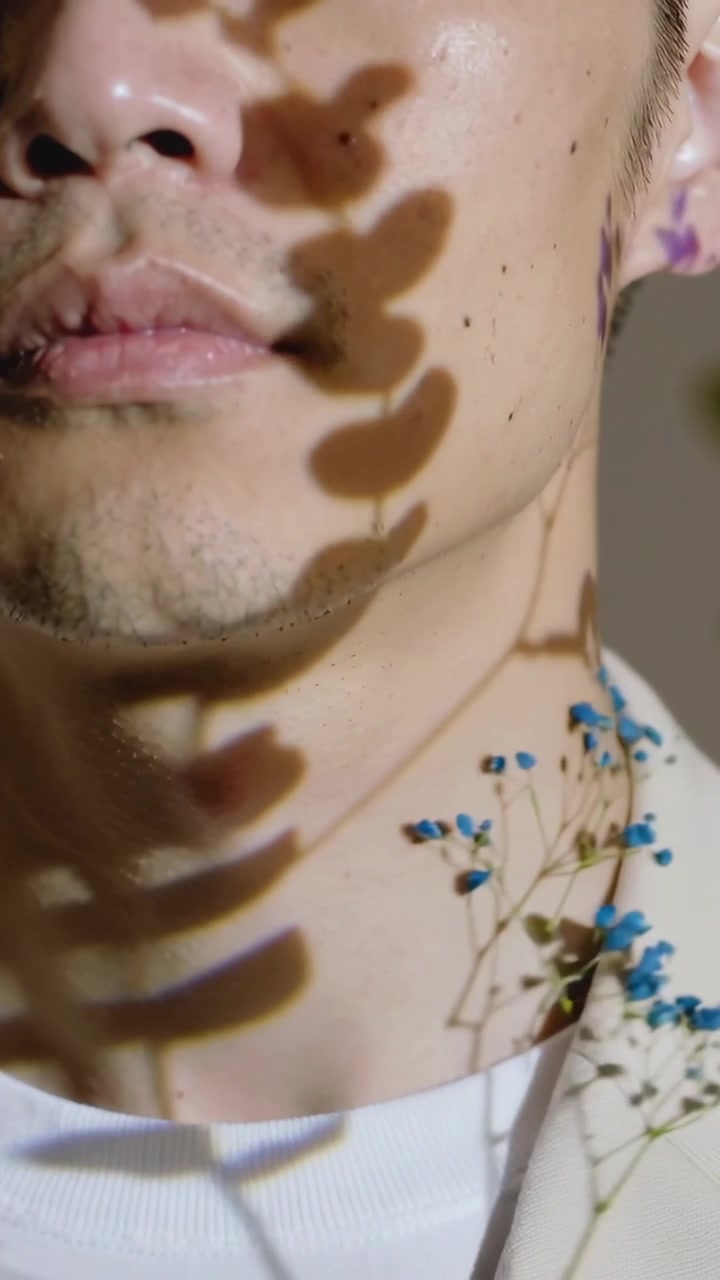 Vertikal video: Bladskygger kastes, mann vipper hodet, lar lyset falle over kjeven i studio, blått blomstermønster.