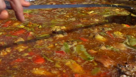 un plato de paella española está siendo mezclado por una mano que sostiene un cucharón de metal, primer plano