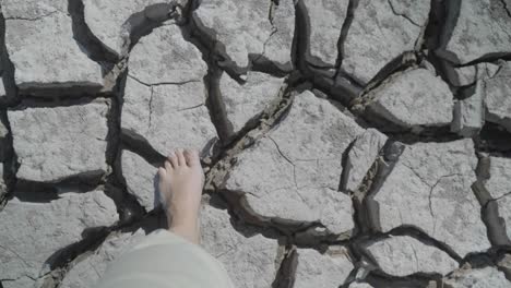 point of view looking down at bare feet walking across dry, cracked land