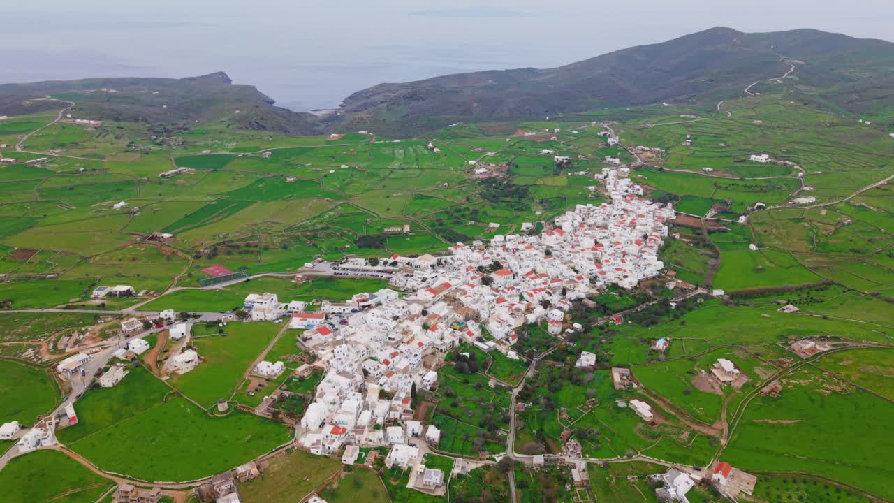Drone panoramic establishing of upper edge of Kythnos town, showing clustered rooftops and rural green hills around