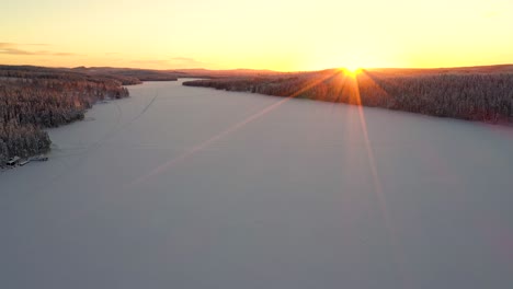 aerial view of sunset over snowy frozen lake in deep forest with hills and mountains