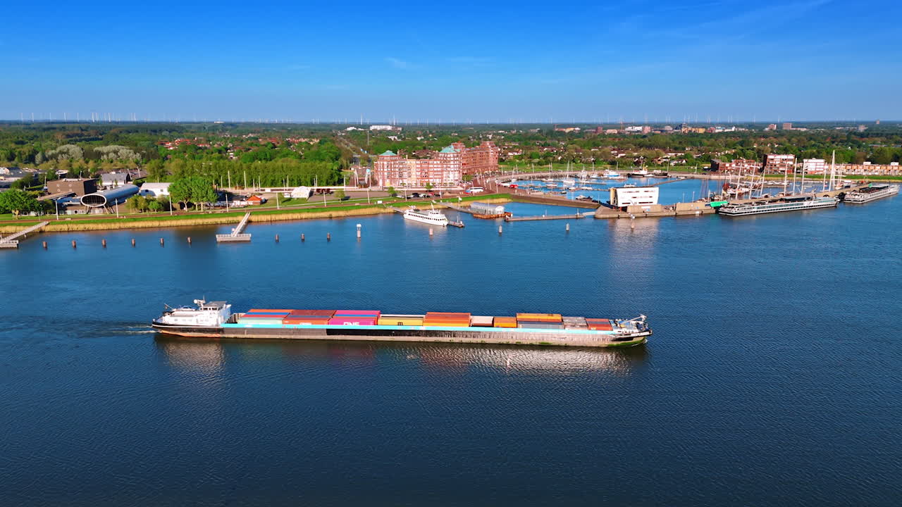 Barge loaded with heavy containers moves by the waterscape of Merkemeer Lake. Scenery of port and cityscape Lelystad, the Netherlands at backdrop. Aerial perspective.