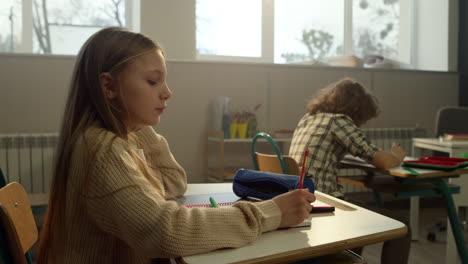 Cheerful-girl-sitting-at-desk-in-school.-Focused-student-learning-in-classroom