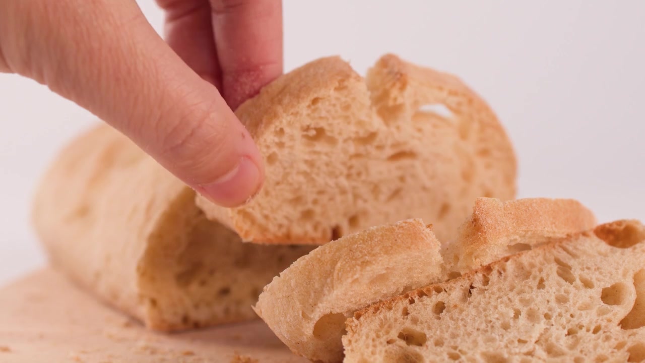 Close-up of hand taking a slice of crusty bread from a wooden board against white.