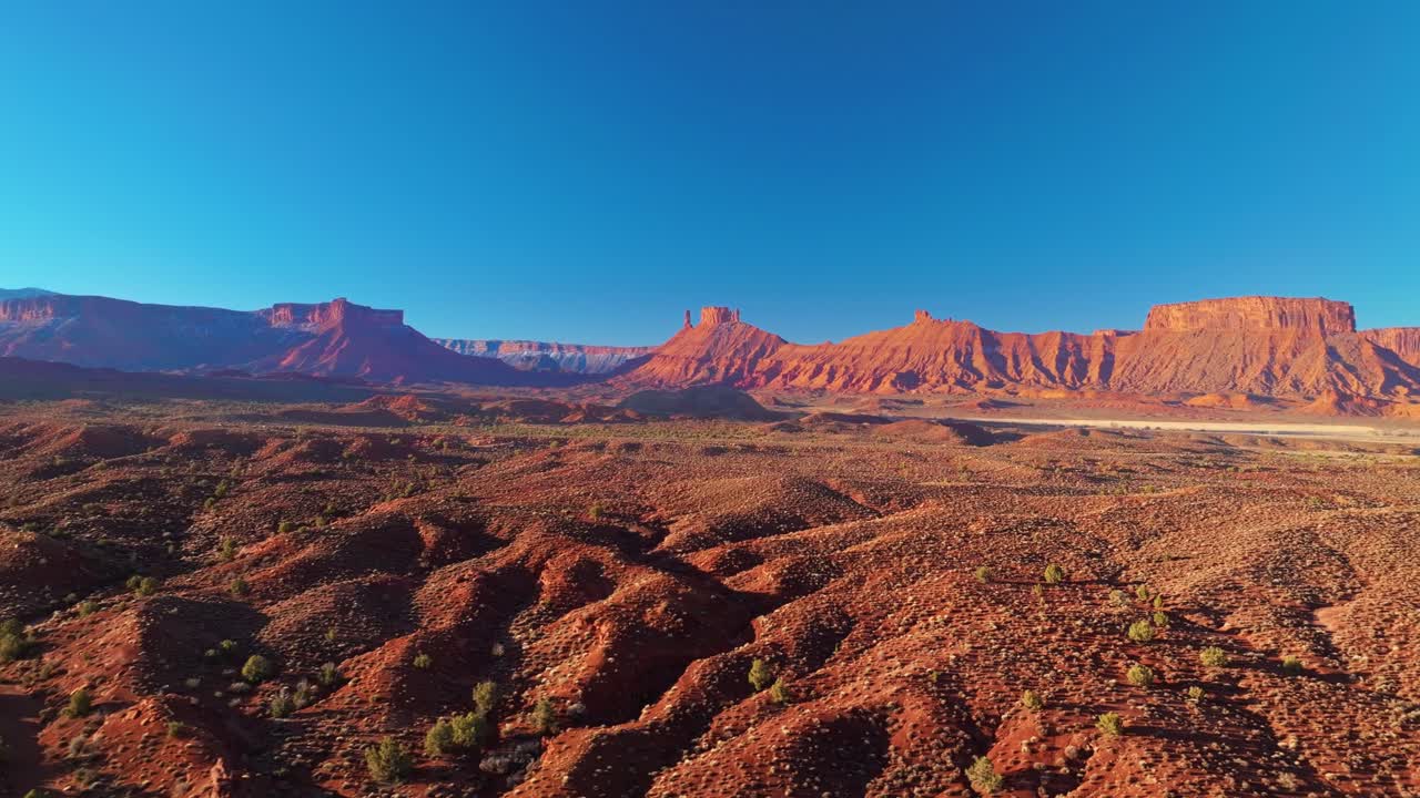 Aerial tracking right establishing of Moab dramatic rock formations, layered sandstone cliffs glowing under midday sunlight