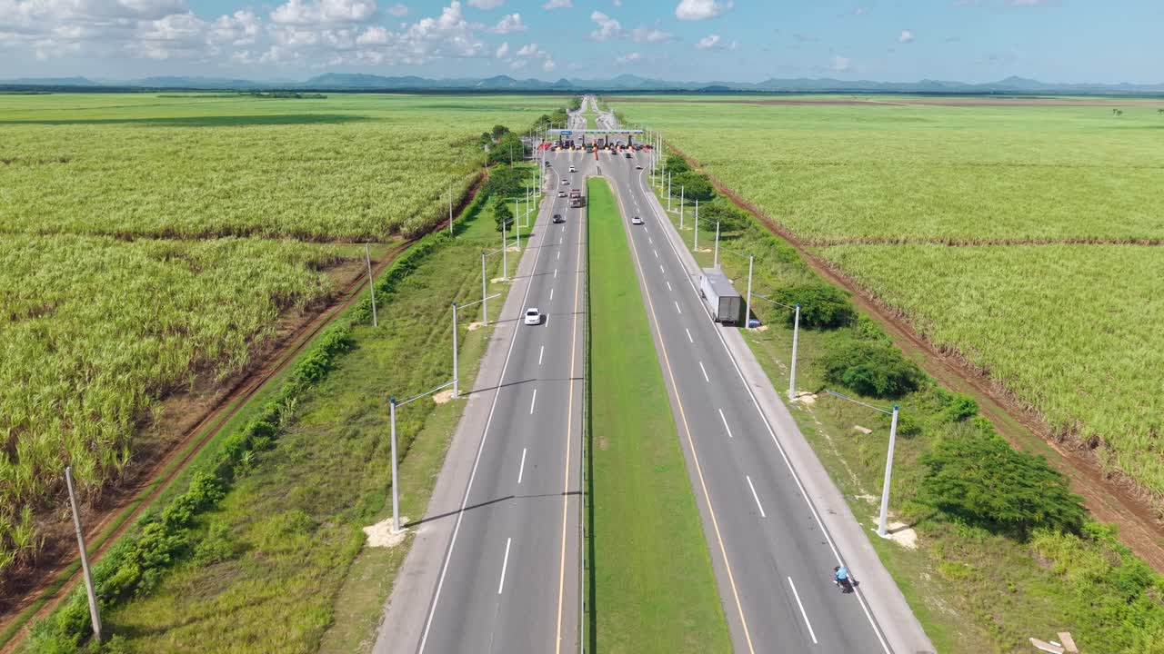 Cars approaching toll booth on Autopista del Coral highway, surrounded by sugarcane fields, Dominican Republic. Aerial forward