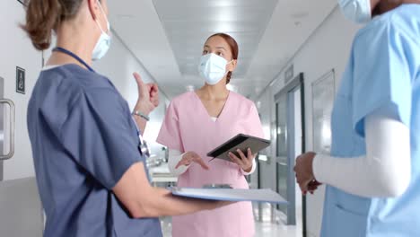 diverse doctors discussing work and using tablet in corridor at hospital, slow motion