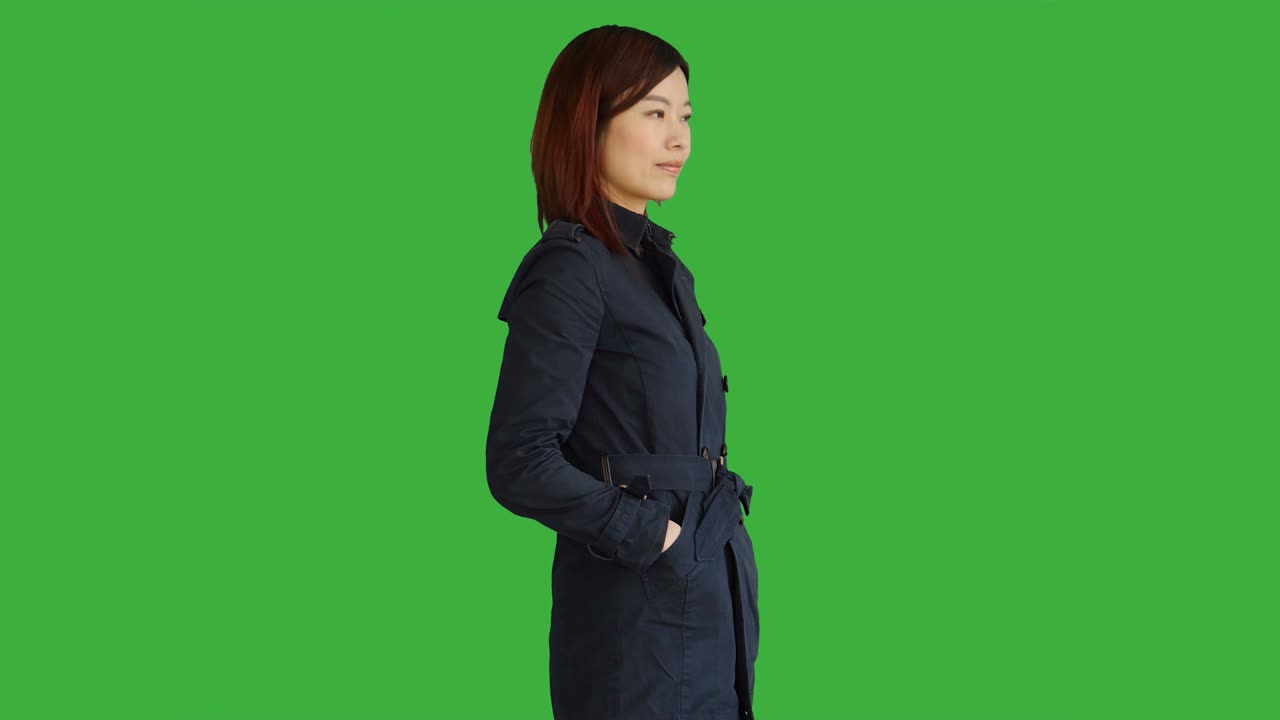 Young Asian Woman Wearing a Blue Coat. Using Smartphone, Digital Tablet and Looking at Camera. Woman Standing in Front of a Green Screen for Chroma Key.