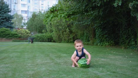 divertido niño pequeño tonto con una sandía en la cámara en el césped verde en el parque