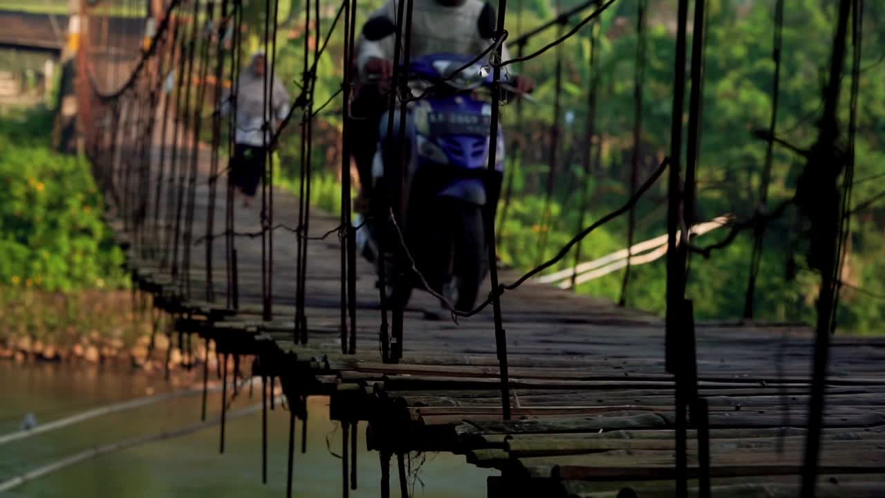la gente y la motocicleta están pasando por el puente colgante de madera