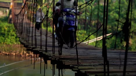 people and motorcycle are passing the wooden suspension bridge