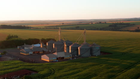 grain silos on a farm at sunset, showcasing open fields and agricultural land, aerial view