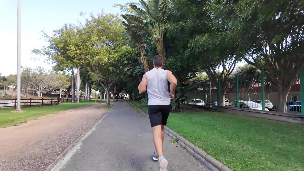 Vista posteriore di un giovane uomo che corre nel parco al rallentatore.