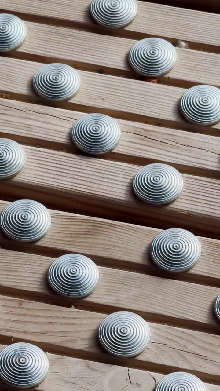 Close-up de degraus de madeira com pinos táteis de metal elevados e sombras iluminadas pelo sol, mostrando detalhes de acesso antiderrapante ao lado de uma instalação de tênis.