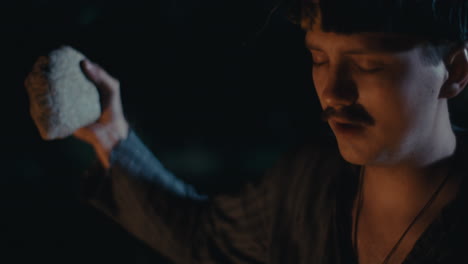 man performing intense ritual with stone by fire at night