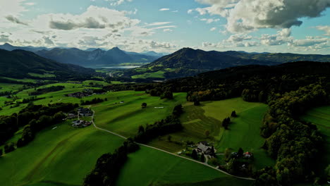 Üppiges-Grünes-Tal-Mit-Verstreuten-Häusern,-Flankiert-Von-Bergen-Unter-Teilweise-Bewölktem-Himmel,-Luftaufnahme