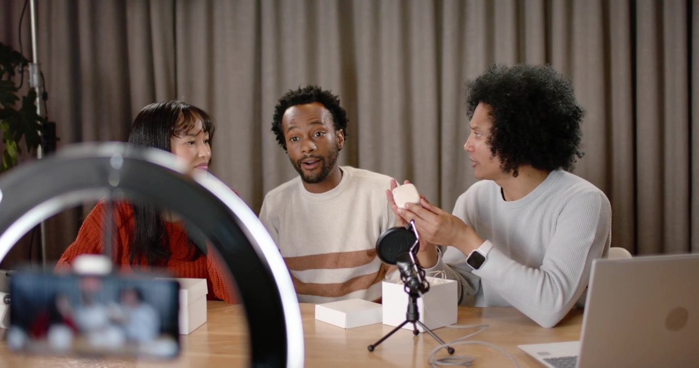 Diverse co-hosts filming on smartphone in ring light, unboxing round device and showing features