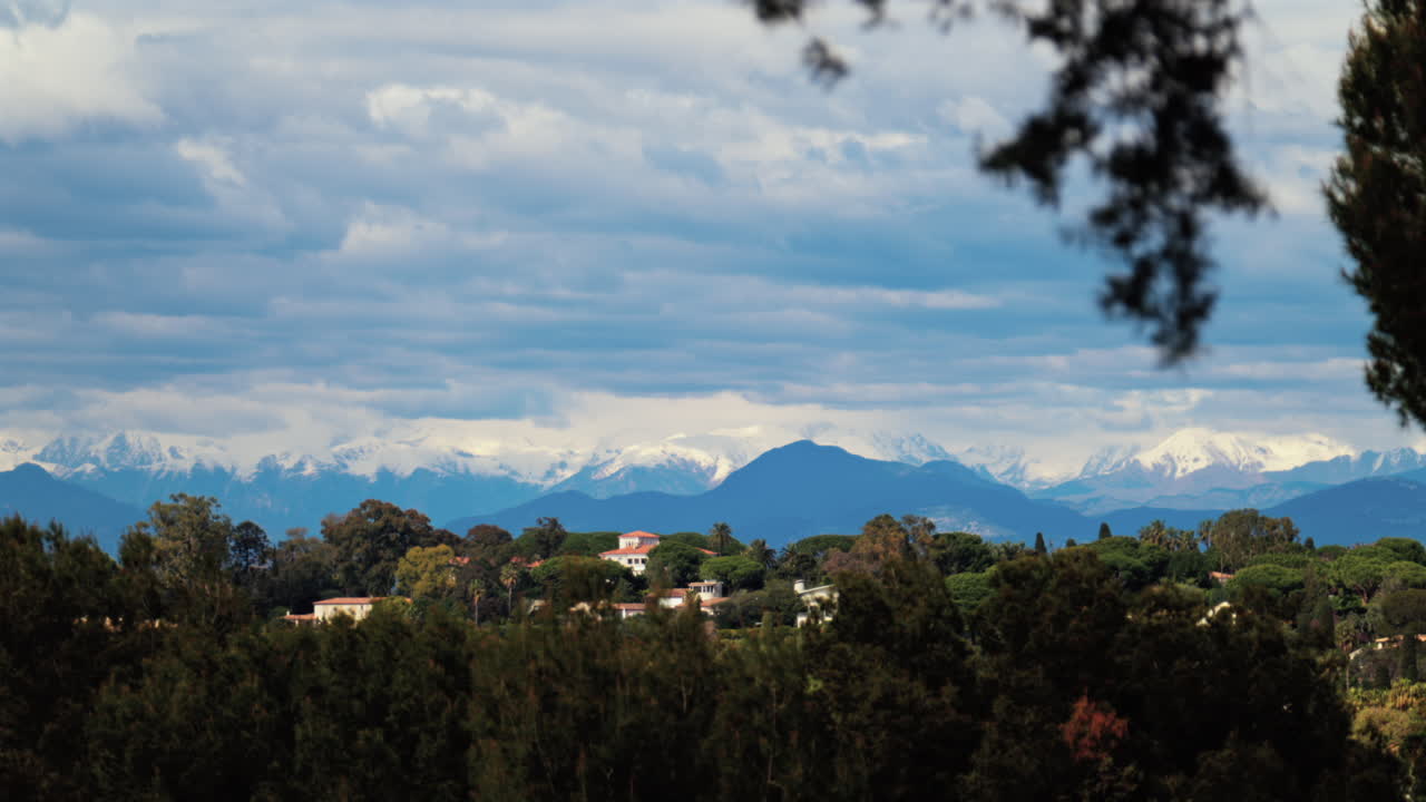 Distant view of orange villas surrounded by green trees with the mountains on the background on a cloudy day