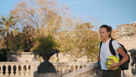 Mujer-Jugadora-De-Fútbol-Con-Mochila-Y-Fútbol-Corriendo-Por-Las-Escaleras-Yendo-A-Un-Entrenamiento-En-El-Parque-De-La-Ciudad.