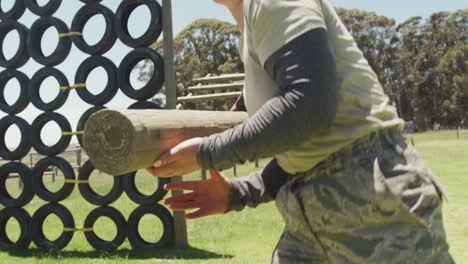 grupo diverso de soldados levantando y llevando troncos de árboles en el sol en el curso de obstáculos del ejército