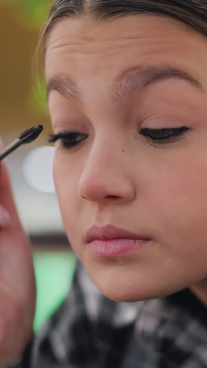 Youth enhancing eye makeup application, Teenager carefully adding mascara to complete her polished appearance, Young woman confidently applies mascara in soft lighting to achieve sophisticated style