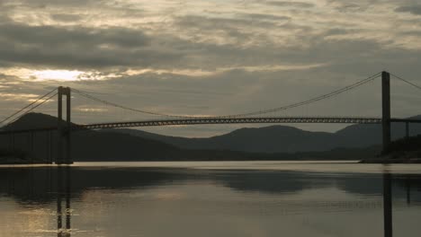 Car-drives-across-a-big-bridge-above-a-river-in-Norway-with-the-sunset-in-the-background