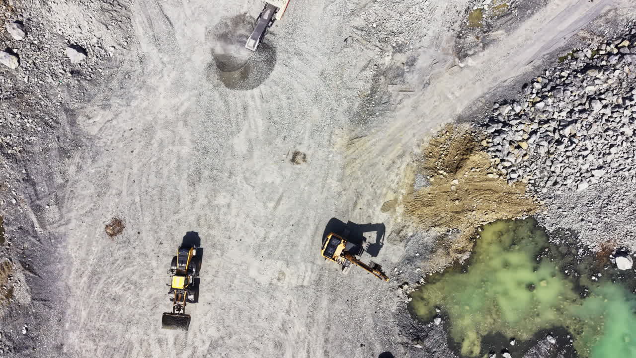 Granite quarry site showing heavy machinery in operation during the day with rocks and water visible in the area