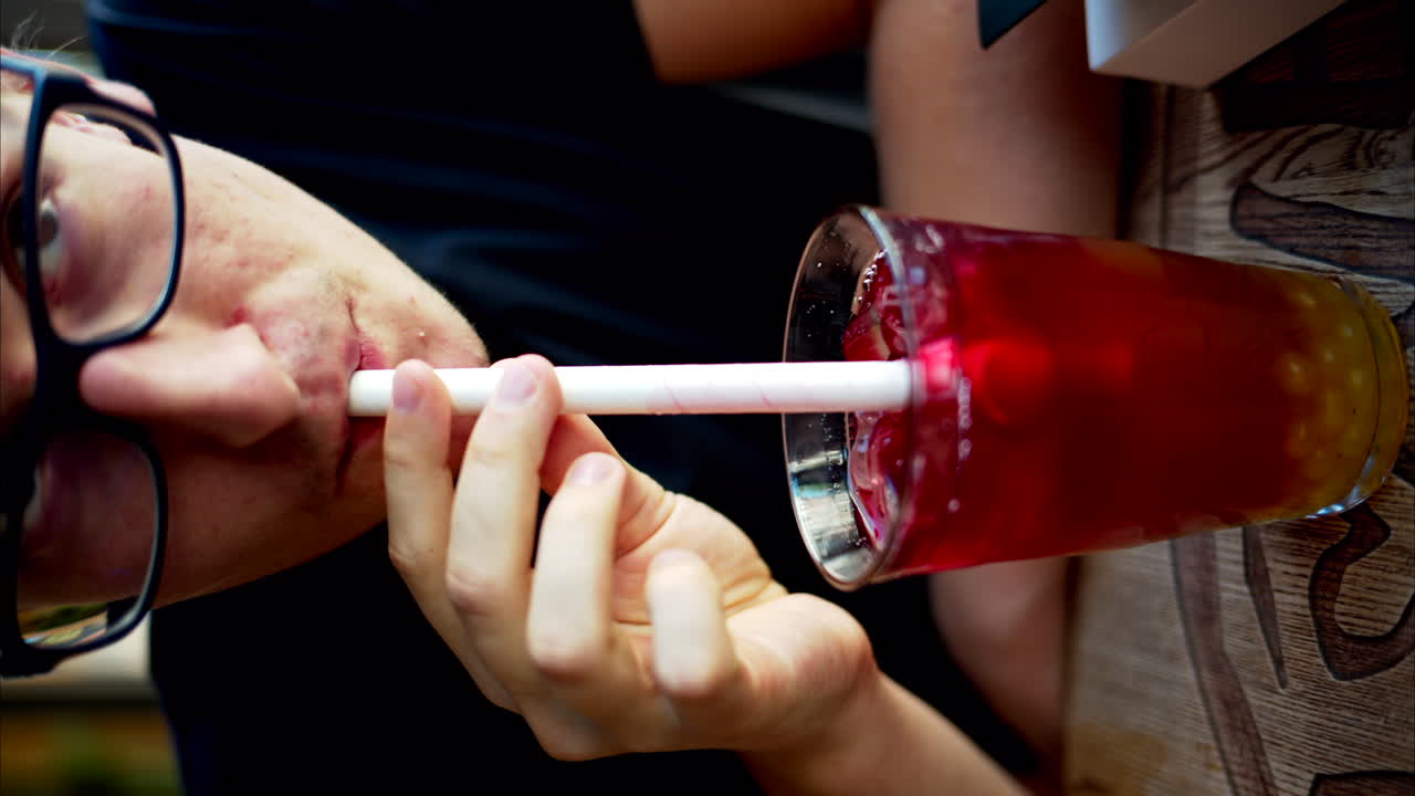 Man drinking red bubble tea with boba in a glass with ice and big white straw close up slow motion, vertical screen