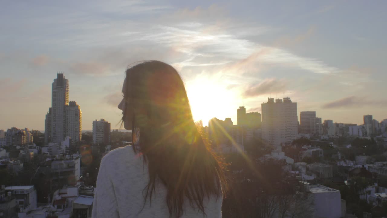 Giovane donna a braccia alzate su un tetto che guarda la città al tramonto