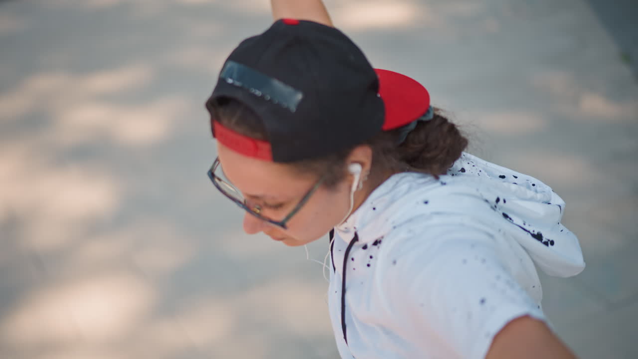 adolescente con gorra al revés, gafas y auriculares, retrato espontáneo en exteriores de un adolescente pensativo ajustándose la gorra mientras escucha música, ligero sudor en la frente, luz del sol al final de la tarde, moteado blanco