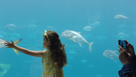 familia en el acuario padre tomando una foto de su hija usando un teléfono inteligente niña disfrutando de mirar peces con su padre compartiendo diversión en el acuario en las redes sociales