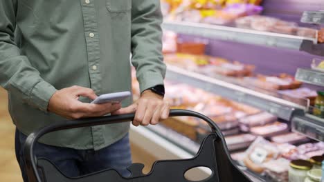 Man-using-mobile-phone-while-shopping-in-supermarket,-trolley-mall-grocery-shot-store