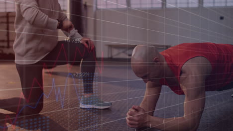 Male client holding plank position in gym, trainer monitoring smartwatch with fitness data charts