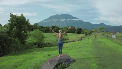 mujer de aventura corriendo descalza en los pasos del campo de hierba en la roca celebrando con los brazos arriba, vista impresionante del gran volcán agung