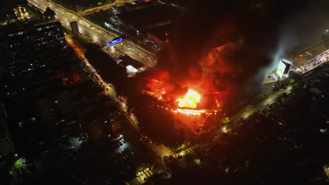drone orbiting the burning exterior of a flaming building, fire raging in a city