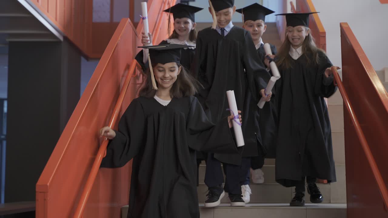 졸업장을 들고 계단을 내려가는 모자와 가운을 입은 미취학 아동 그룹 중 한 명이 교사를 껴안고 있습니다.