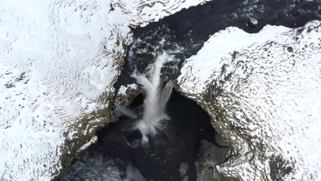 AERIAL:-Close-Up-of-Waterfall-in-Snow,-Ice-Canyon-in-Iceland-Green-Grass,-Cloudy