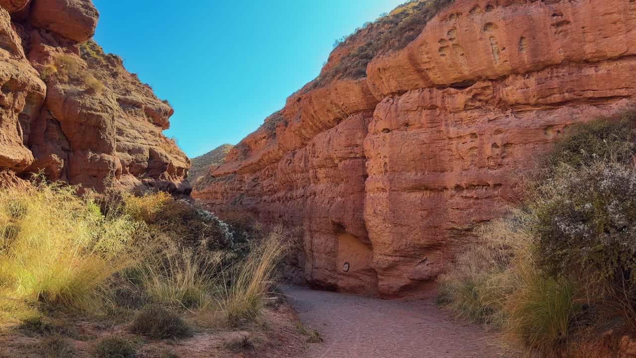 Pingshan Lake Grand Canyon, Zhangye, provincia di Gansu, Cina - Strette pareti del canyon di arenaria rossa racchiudono un sentiero tortuoso sotto un cielo luminoso e senza nuvole - Panoramica a sinistra