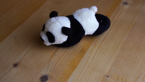 black white small toy panda bear lies on a wooden table and rotates