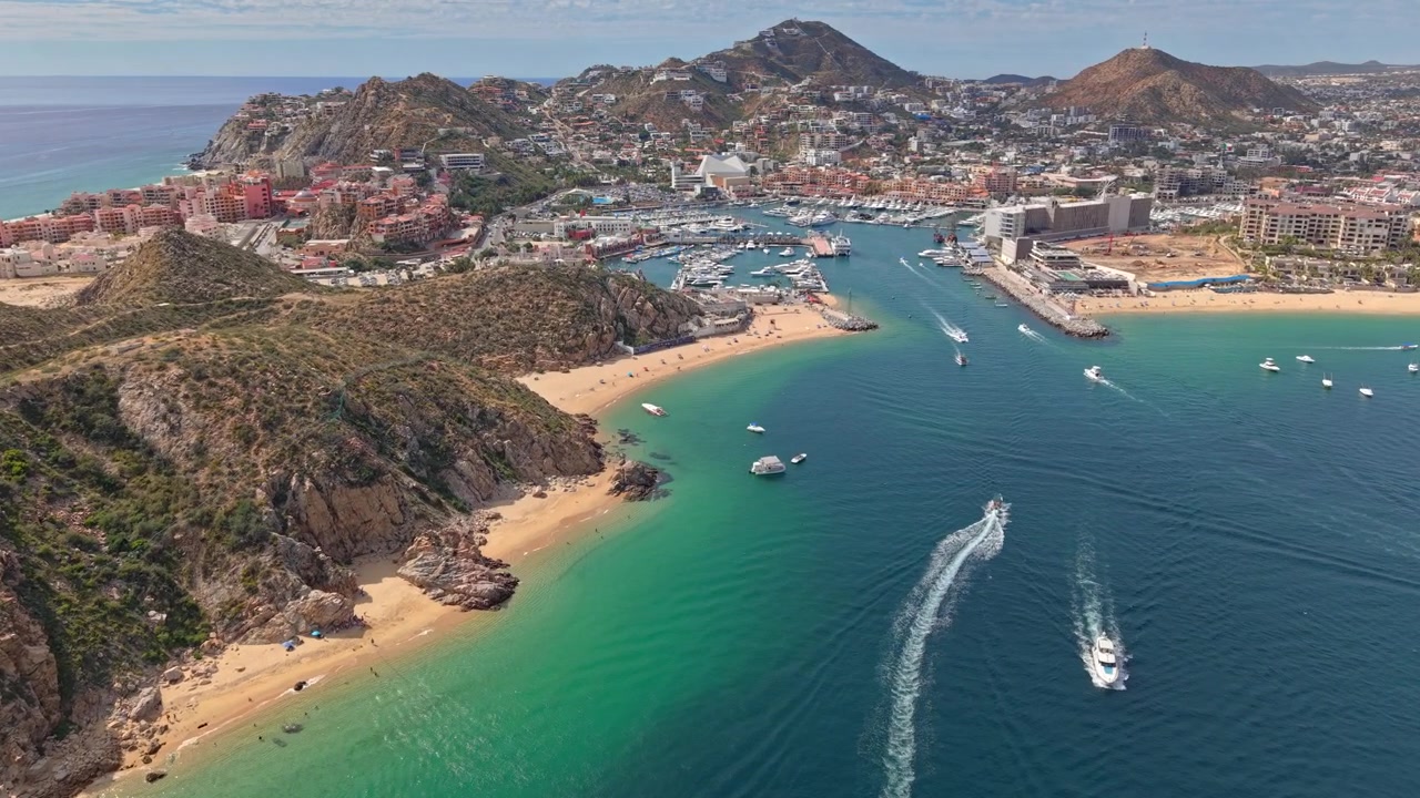 Vista aérea de uma aproximação em dolly da baía de Cabo San Lucas, apresentando o porto e iates de luxo, juntamente com arquitetura acolhedora para turistas em um dia ensolarado, Baja California, México