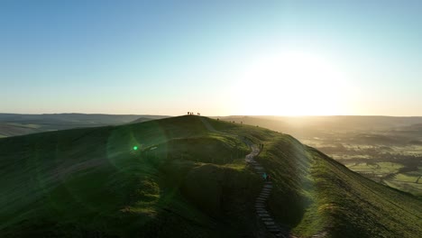 dramática toma de órbita aérea de la gente de pie encima de mam tor en el punto trigonométrico viendo el amanecer en el distrito del pico, reino unido