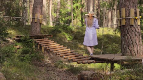 girl wearing summery clothes attempts to climb wobbly bridge at park forest