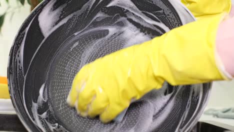 person wearing yellow gloves washing a frying pan