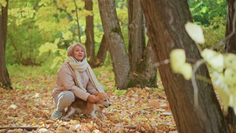 smiling woman cuddling beagle puppy among golden autumn leaves in deciduous forest, kneeling on colourful leaf carpet between mossy trunks, enjoying playful bonding amid tranquil nature