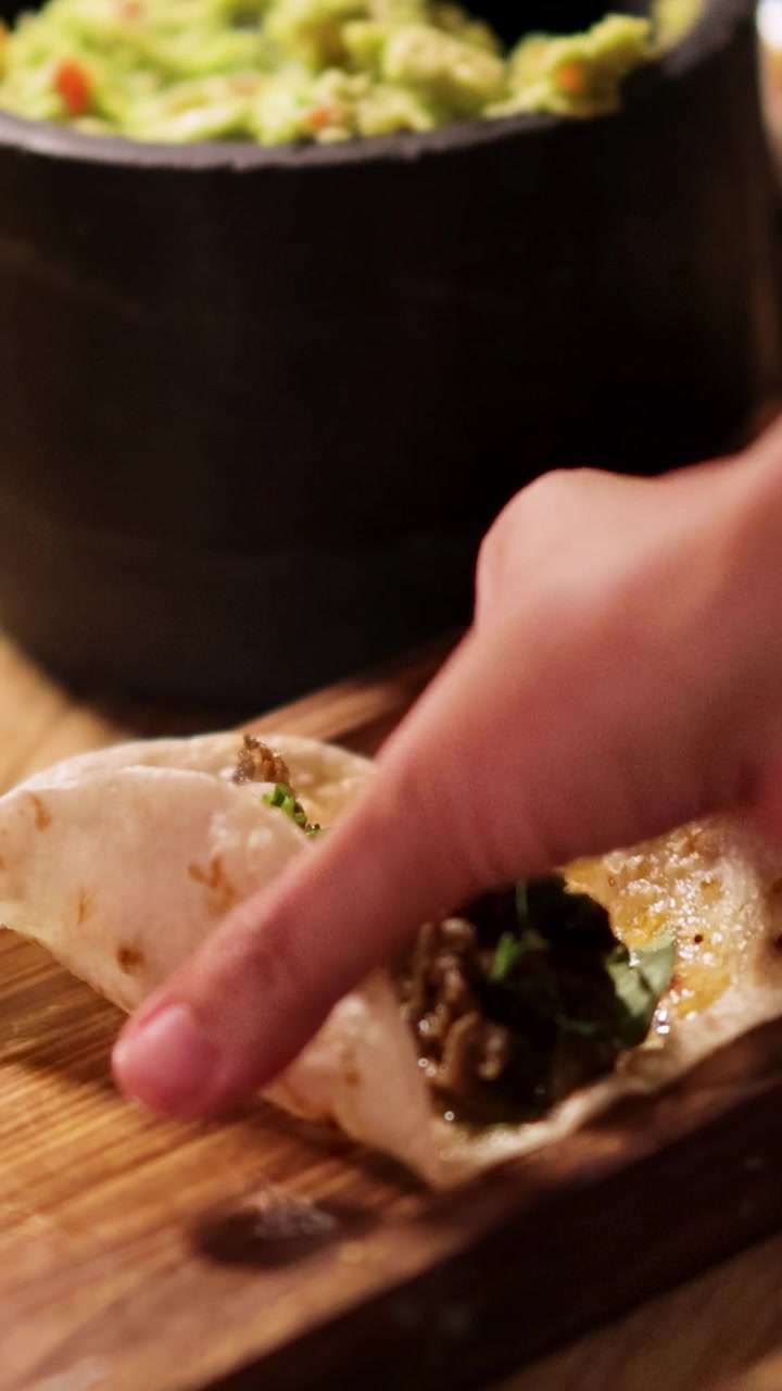 En hånd tager en taco fra et træbræt i et svagt oplyst restaurantmiljø.