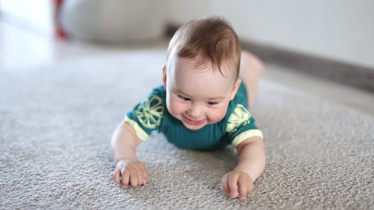 Cheerful happy Caucasian baby boy lies on belly smiling. Adorable child banging his limbs over the floor actively.