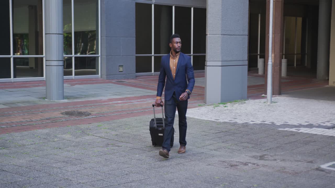 African american businessman walking with suitcase in city street